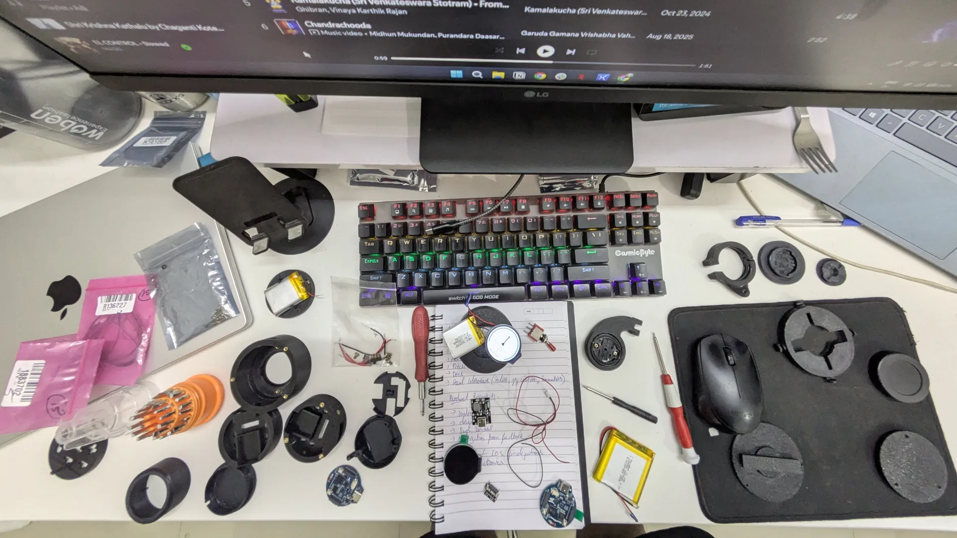 Overhead view of the desk mid-build — housings, boards, batteries and tools spread out around a notebook